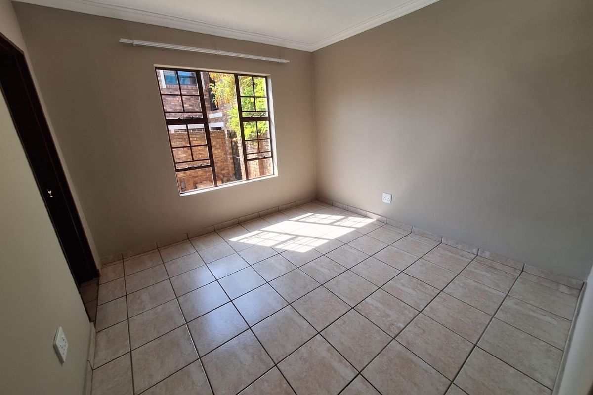 A bright, empty bedroom featuring neutral wall paint, tiled flooring, and a window fitted with security bars.