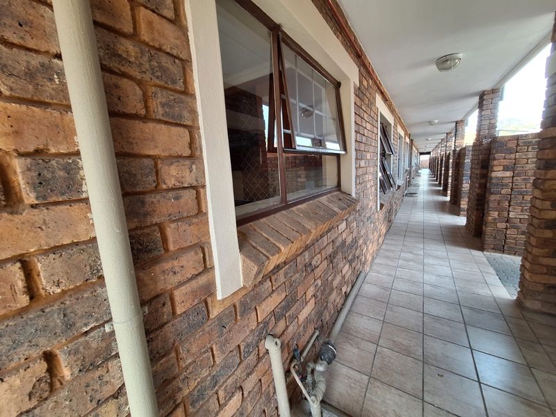 A long, covered exterior walkway featuring exposed brick walls, tiled flooring, and multiple top-hung windows along the townhouse facade.