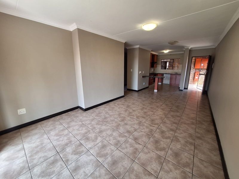 Spacious open-plan living area featuring tiled flooring, flowing into a functional kitchen with built-in cabinetry and a breakfast bar.