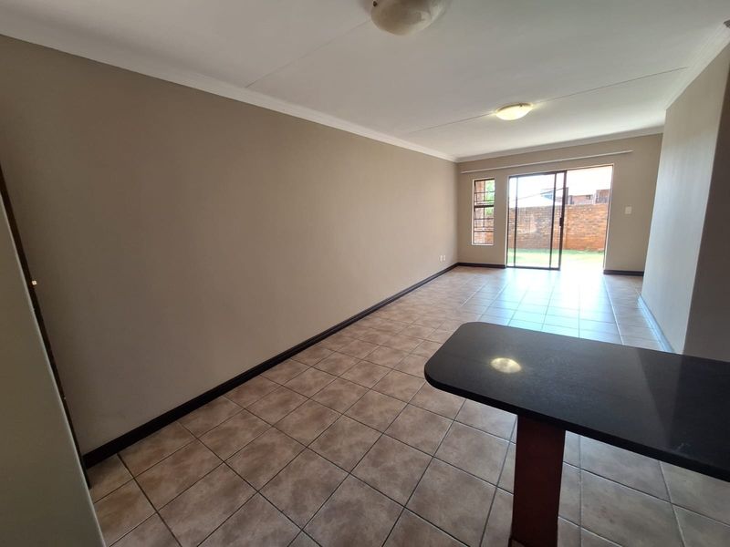 Spacious open-plan living area featuring neutral walls, tiled flooring, and a breakfast counter, with direct access to the rear garden through a sliding door.