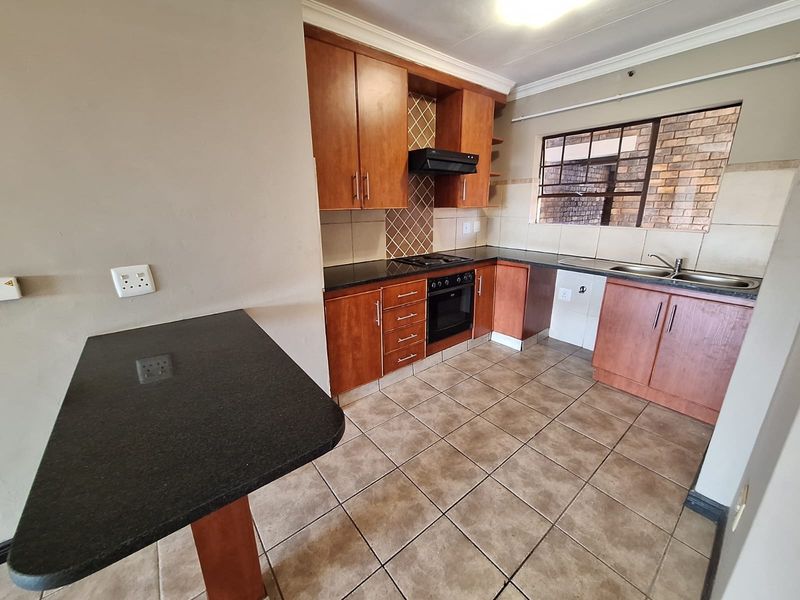 A functional kitchen featuring wooden cabinetry, granite countertops, built-in oven, hob, extractor fan, and a breakfast bar, with tiled flooring throughout.