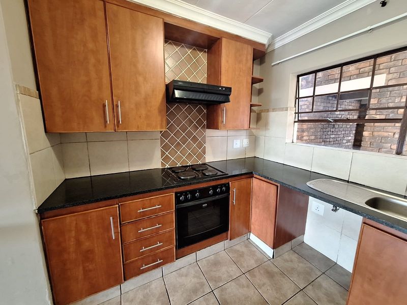 Functional kitchen featuring wooden cabinetry, black granite countertops, built-in oven with hob, extractor fan, and tiled flooring.