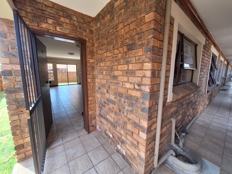 Entrance area of a townhouse featuring face brick exterior, tiled flooring, and a security gate leading into an open-plan living space.