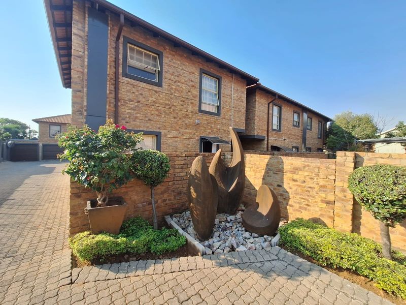 A well-maintained townhouse exterior featuring a face brick facade, paved driveway, and a landscaped front garden area with a decorative stone feature.
