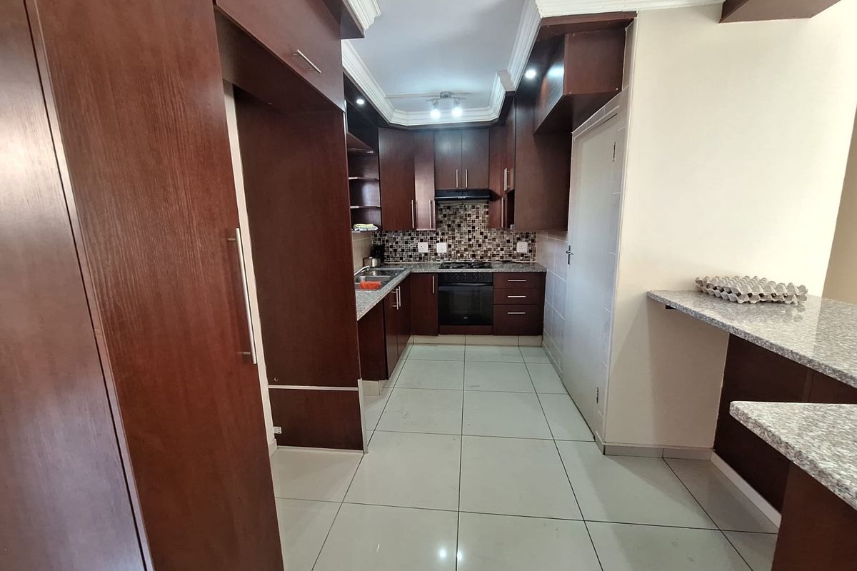 A functional kitchen featuring dark wood cabinetry, granite countertops, a mosaic backsplash, and integrated appliances, including a built-in oven and hob.