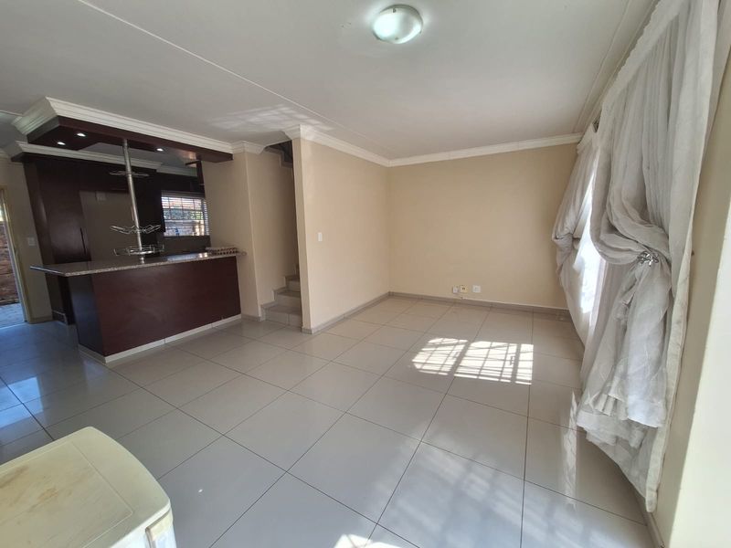 Spacious open-plan living area featuring tiled flooring, a breakfast bar with built-in cabinetry, and a staircase leading to the upper level.