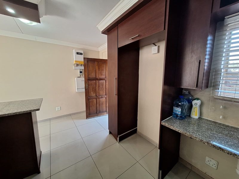 A functional kitchen area featuring dark wood cabinetry, granite countertops, tiled flooring, and a wall-mounted solar inverter system.