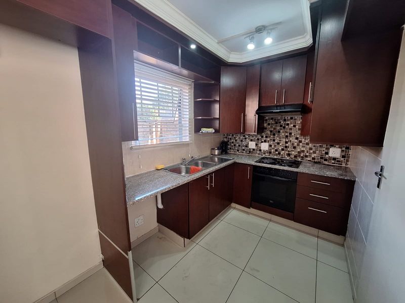 A functional kitchen featuring dark wood cabinetry, granite countertops, a built-in oven with hob, and a tiled backsplash.