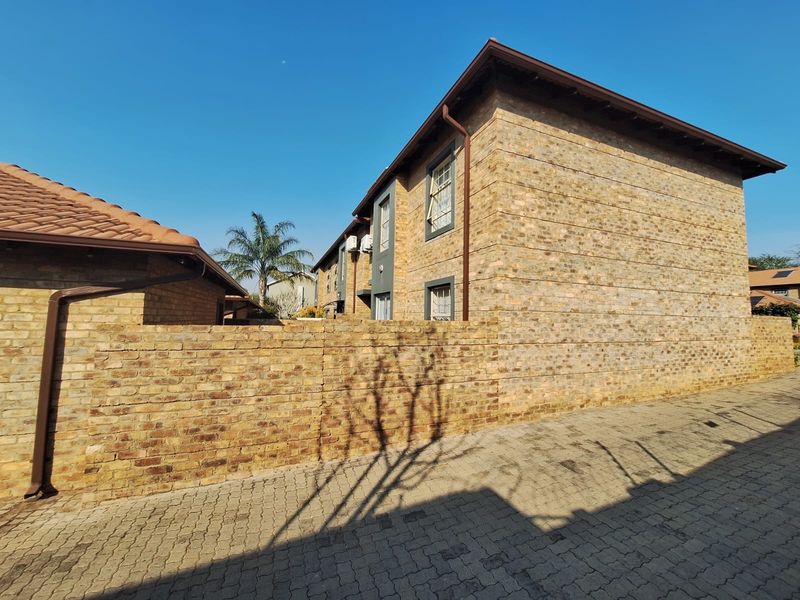 A view of the townhouse exterior featuring face brick construction, a paved driveway, and a secure boundary wall.