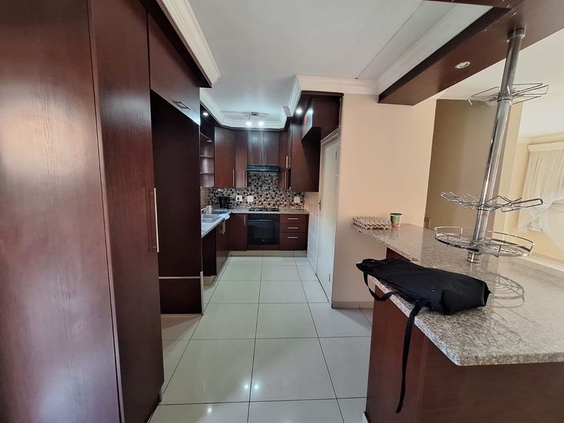 A functional kitchen featuring dark wood cabinetry, granite countertops, a breakfast bar, and a mosaic tile backsplash with integrated oven and hob.