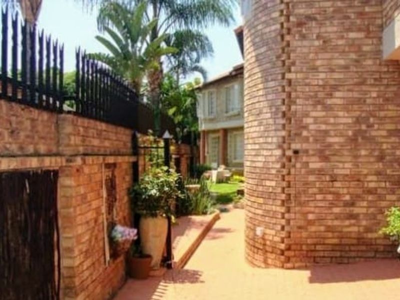 A side pathway featuring face brick walls, curved architectural detailing, and metal security fencing leading towards the rear garden area.
