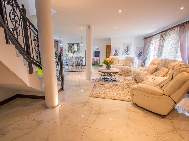 Spacious open-plan living and dining area featuring polished marble-look floor tiles, structural columns, and a decorative wrought iron staircase.