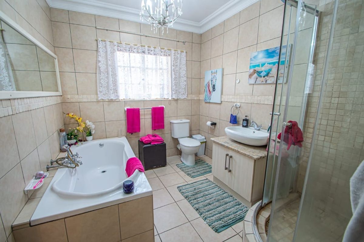 A functional bathroom featuring a built-in bathtub, separate shower enclosure, vanity cabinet with basin, and neutral wall and floor tiling.