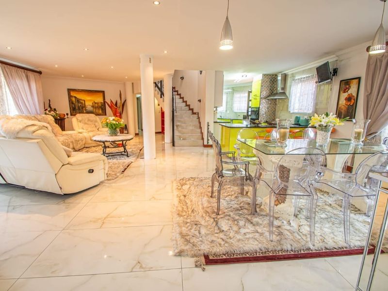 Spacious open-plan living, dining, and kitchen area featuring polished porcelain tile flooring, modern recessed lighting, and a central staircase.