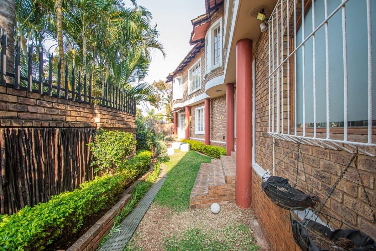 A side garden pathway featuring a brick facade, security-barred windows, and a landscaped garden area with a brick boundary wall.