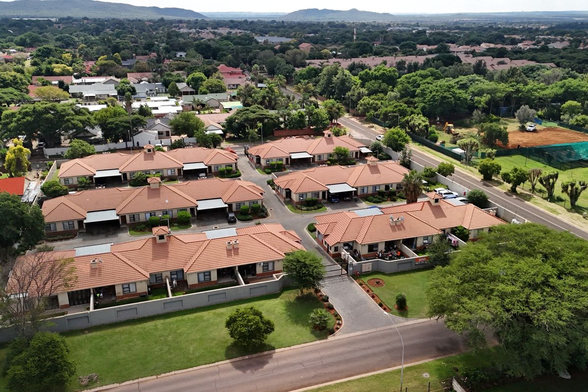 Aerial view of a residential townhouse complex featuring tiled roofs, paved driveways, and well-maintained communal garden areas within a secure estate.