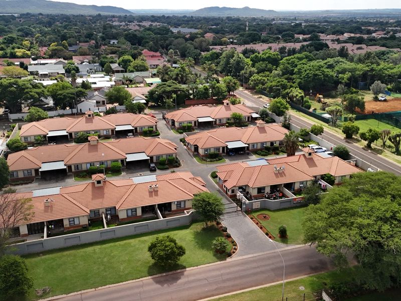 Aerial view of a residential townhouse complex featuring tiled roofs, paved driveways, and well-maintained communal garden areas within a secure estate.