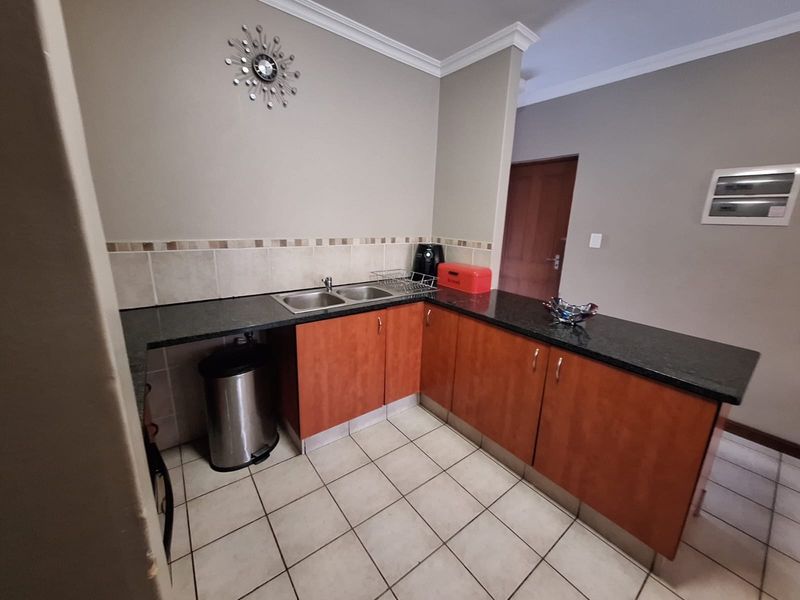 A functional kitchen featuring granite countertops, double basin sink, tiled backsplash, and warm-toned laminate cabinetry with ceramic floor tiles.