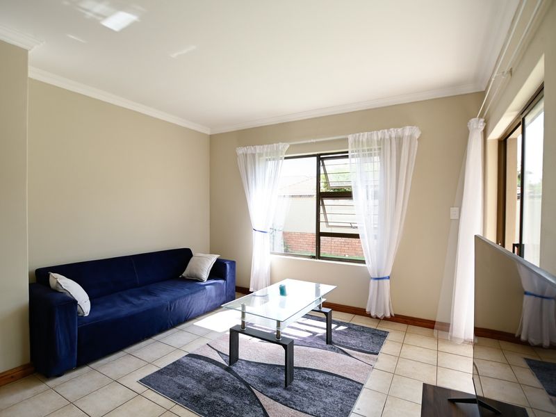 A bright living room featuring tiled flooring, neutral walls, and natural light through a large window and sliding door access.