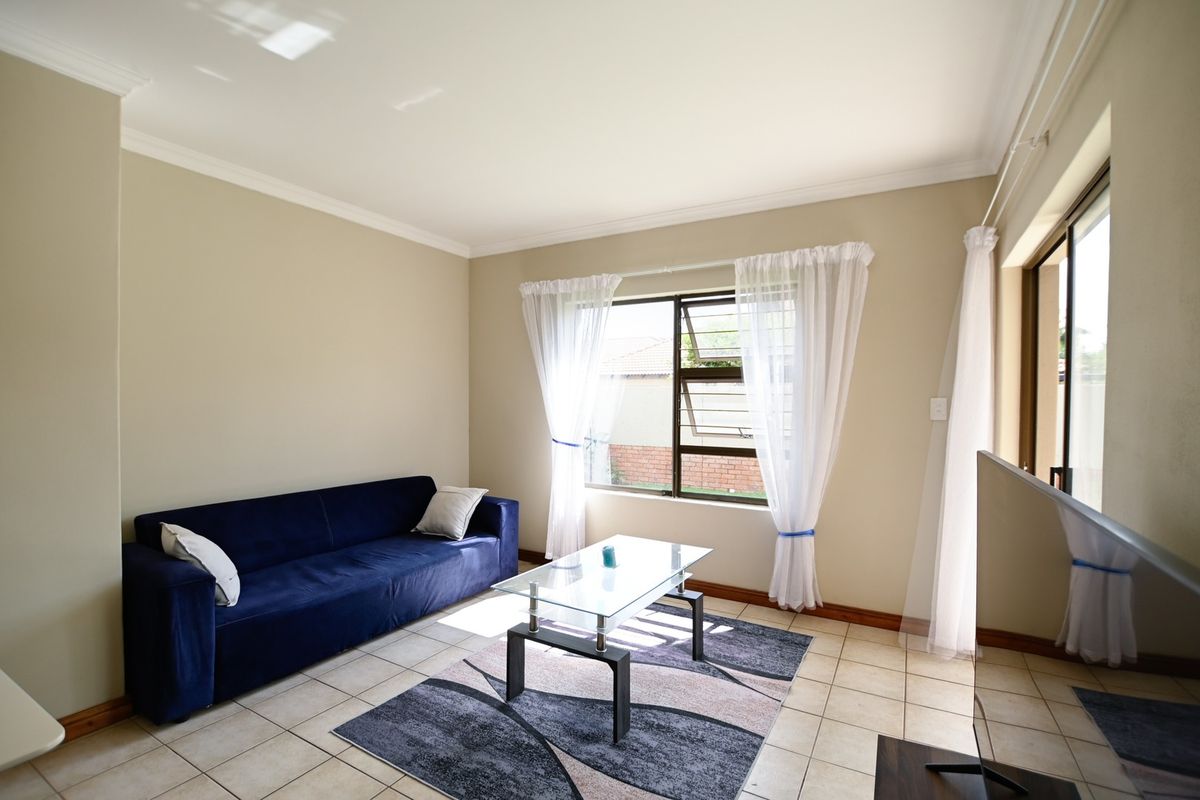 A bright living room featuring tiled flooring, neutral walls, and natural light through a large window and sliding door access.
