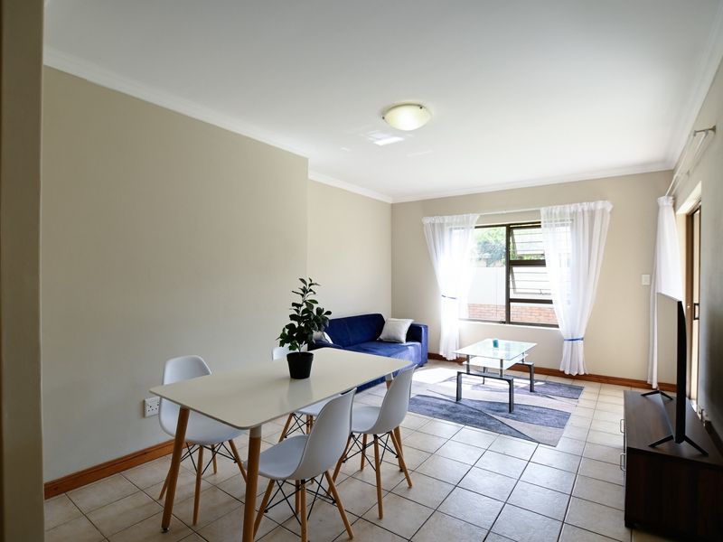An open-plan living and dining area featuring neutral wall tones, tiled flooring, and natural light through an aluminium-framed window.