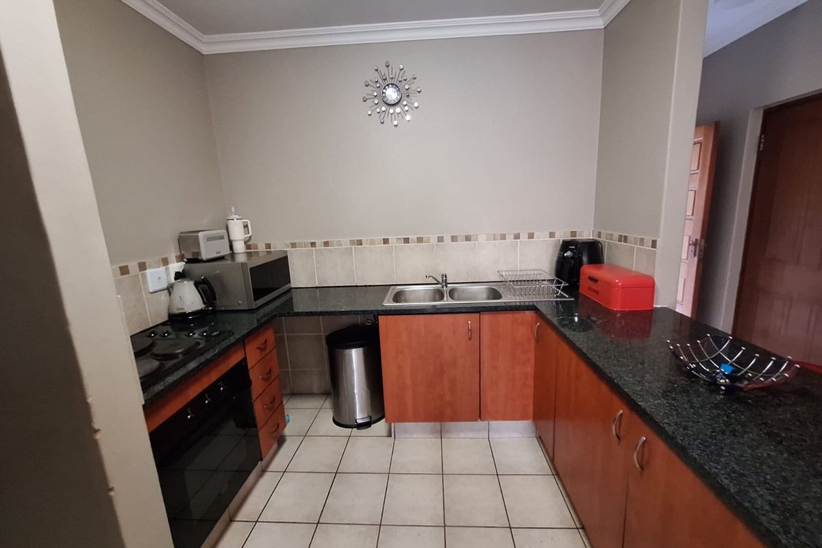 Functional kitchen featuring granite countertops, built-in oven, electric hob, double sink, and ample laminate cabinetry with tiled flooring.