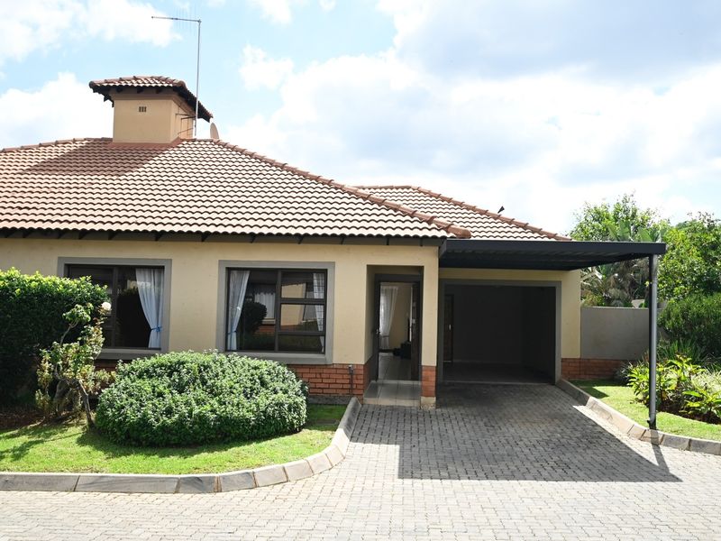 Front elevation of a townhouse featuring a tiled roof, brick accents, paved driveway, and an integrated carport.
