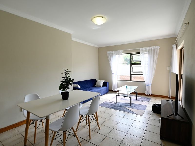 An open-plan living and dining area featuring neutral wall tones, tiled flooring, and natural light through a large window and sliding door.