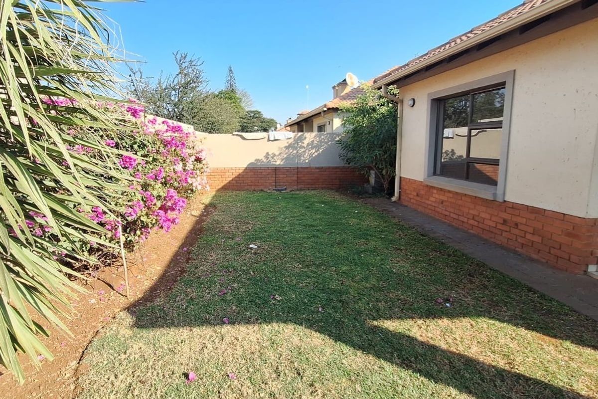 A private rear garden featuring a lawn area, established bougainvillea, and a brick boundary wall adjacent to the townhouse exterior.