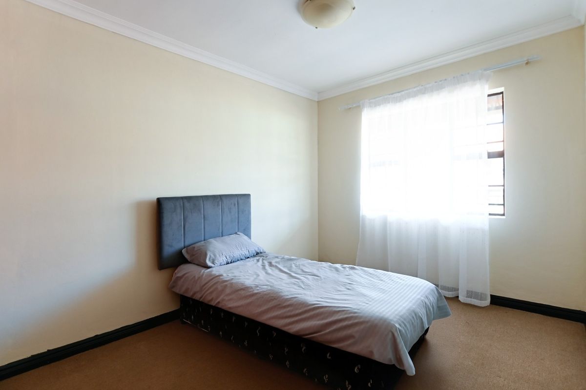 A simple bedroom featuring neutral walls, carpeted flooring, and a window with a curtain rail.