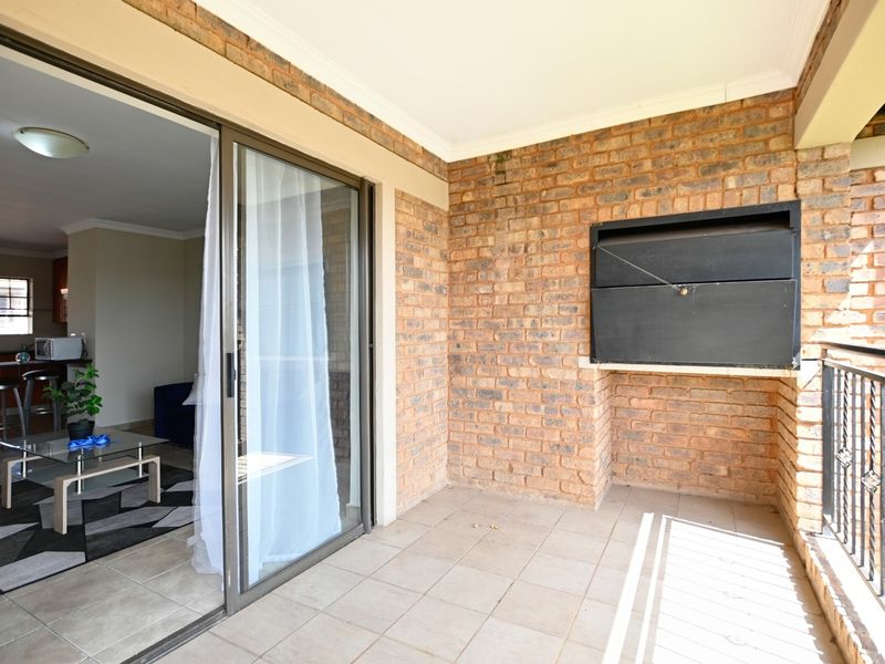 Covered balcony featuring a built-in braai, tiled flooring, and sliding door access to the interior living area.