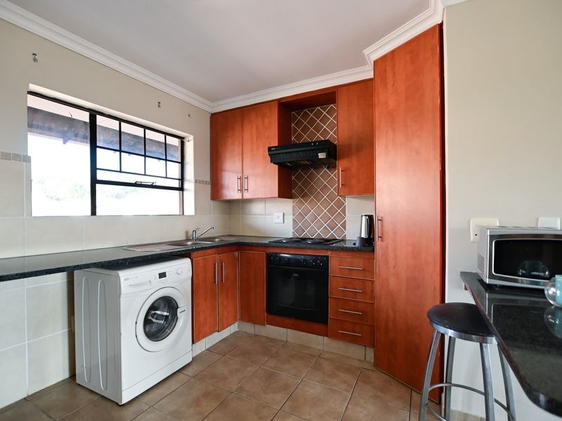 Compact kitchen featuring wooden cabinetry, granite countertops, built-in oven, hob, extractor fan, and tiled flooring with integrated laundry space.