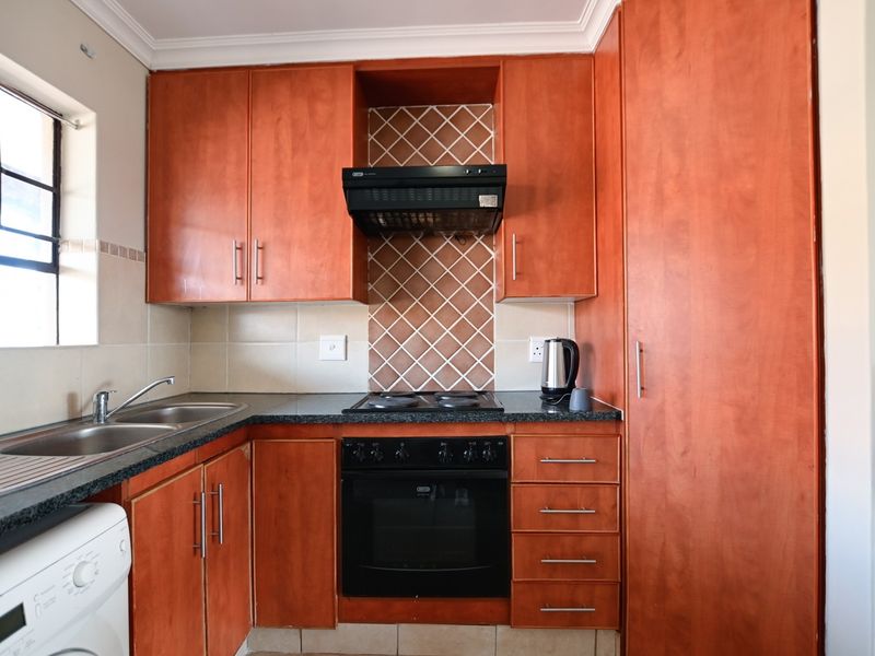 A functional kitchen featuring wood-finish cabinetry, granite countertops, a built-in oven with hob, extractor fan, and a double sink with tiled backsplash.