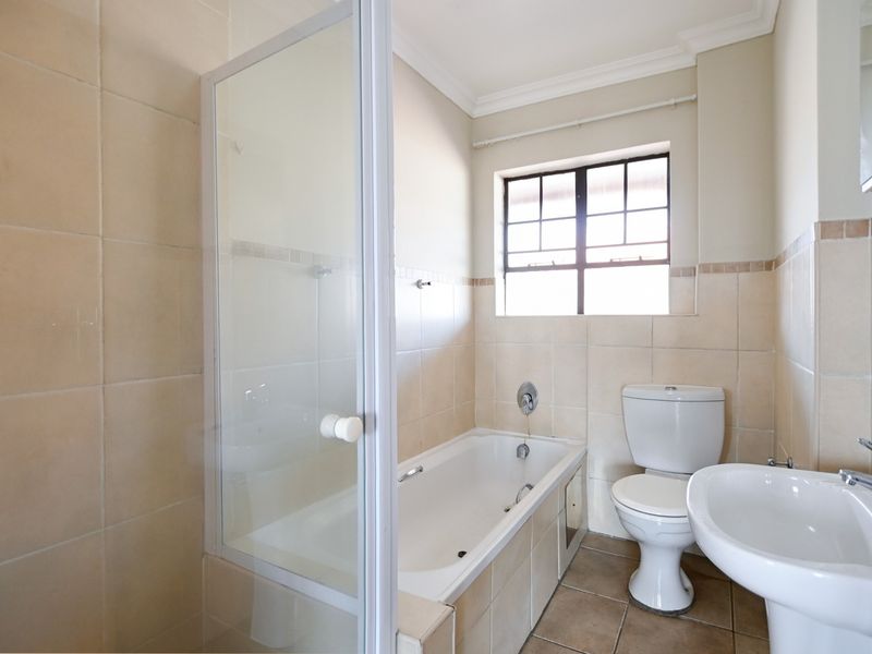 A functional bathroom featuring a built-in bathtub with a glass shower screen, a pedestal washbasin, and a ceramic toilet with neutral wall tiling.