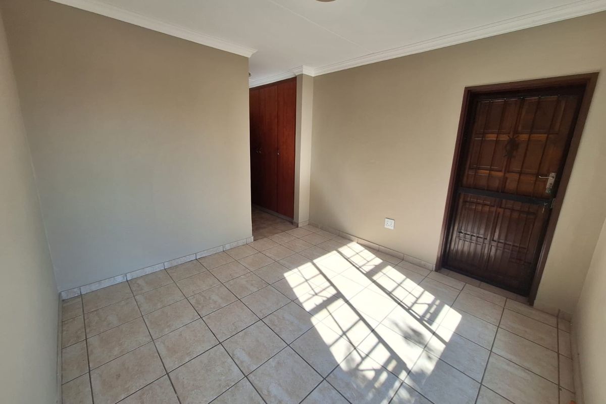 An empty bedroom featuring neutral wall paint, tiled flooring, built-in wooden cupboards, and a solid wooden door.
