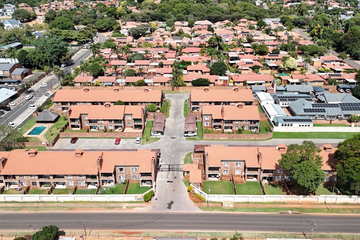 Aerial view of a residential townhouse complex featuring multiple brick buildings with tiled roofs, communal parking, and a swimming pool.