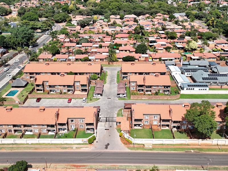 Aerial view of a residential townhouse complex featuring multiple brick buildings with tiled roofs, communal parking, and a swimming pool.