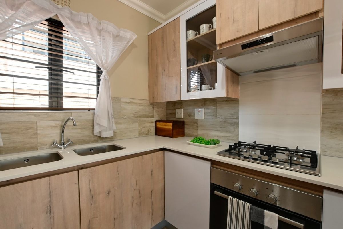 Modern kitchen featuring light wood-finish cabinetry, stone countertops, a gas hob with extractor fan, and a stainless steel double sink.