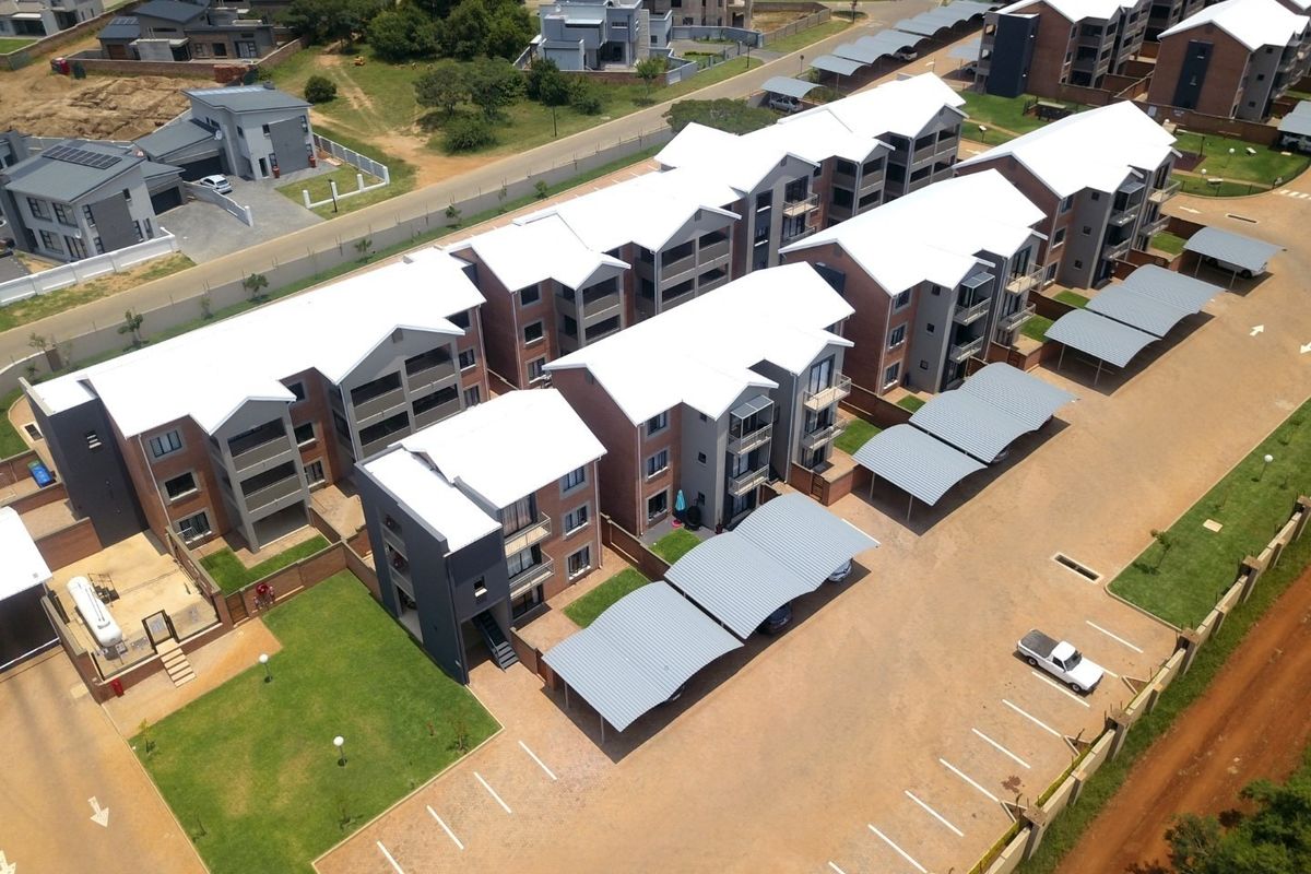 Aerial view of a modern apartment complex featuring multiple residential blocks, covered parking bays, and landscaped communal grounds.