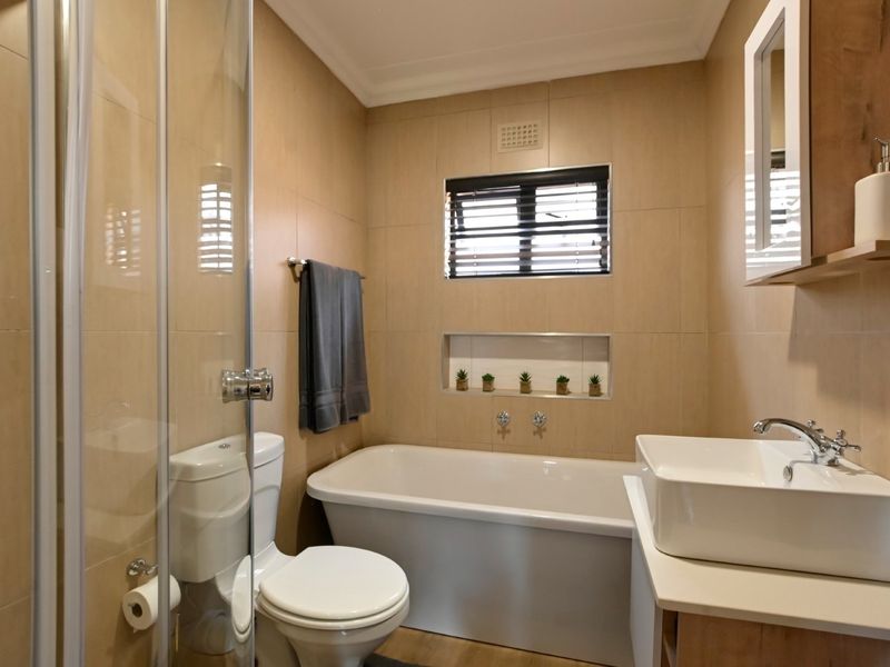 A modern bathroom featuring a glass-enclosed shower, a bathtub, a vessel sink vanity, and neutral wall tiling with a built-in storage niche.
