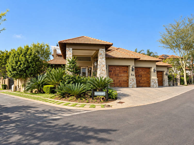 A well-maintained front elevation featuring a triple garage, stone-clad pillars, tiled roof, and established landscaped garden in a secure estate setting.