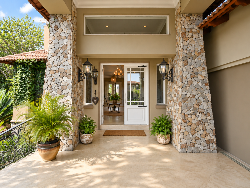 Inviting front entrance featuring stone-clad pillars, elegant wrought iron railings, and a classic French door entry with a transom window.