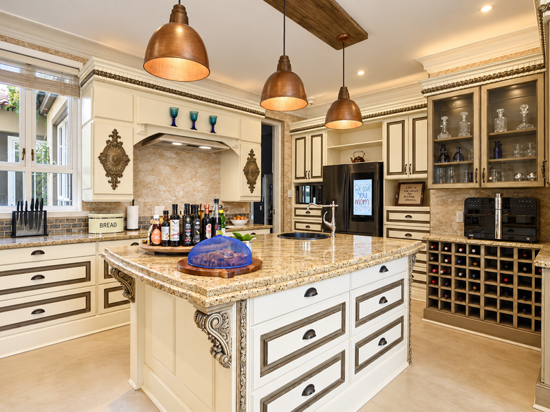 A well-appointed kitchen featuring a large granite-topped island, custom cabinetry with glass-front displays, built-in wine storage, and elegant pendant lighting.