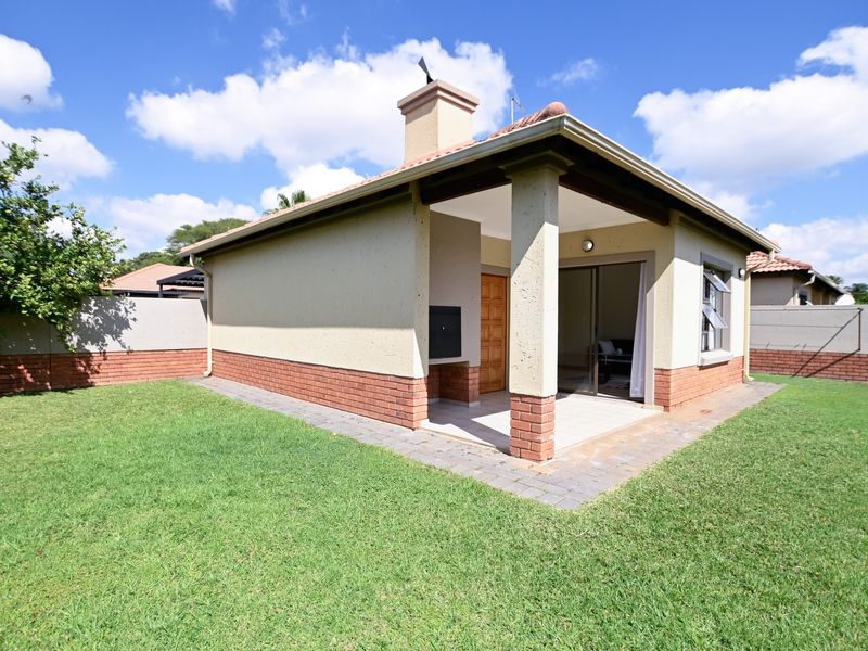 Rear view of the townhouse featuring a covered patio with a built-in braai, tiled roof, and a private garden with brick boundary walls.