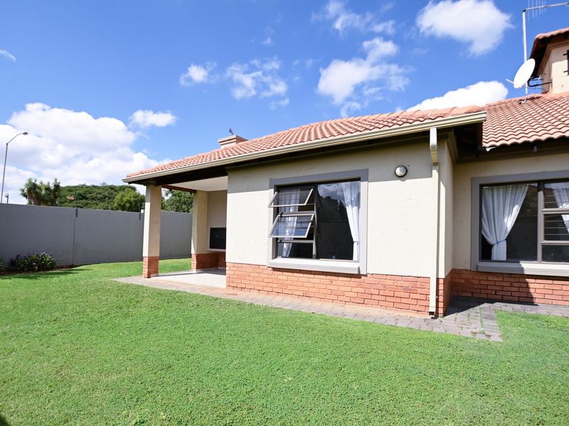 Rear view of the townhouse featuring a covered patio with a built-in braai, brick and plaster facade, and a well-maintained garden.