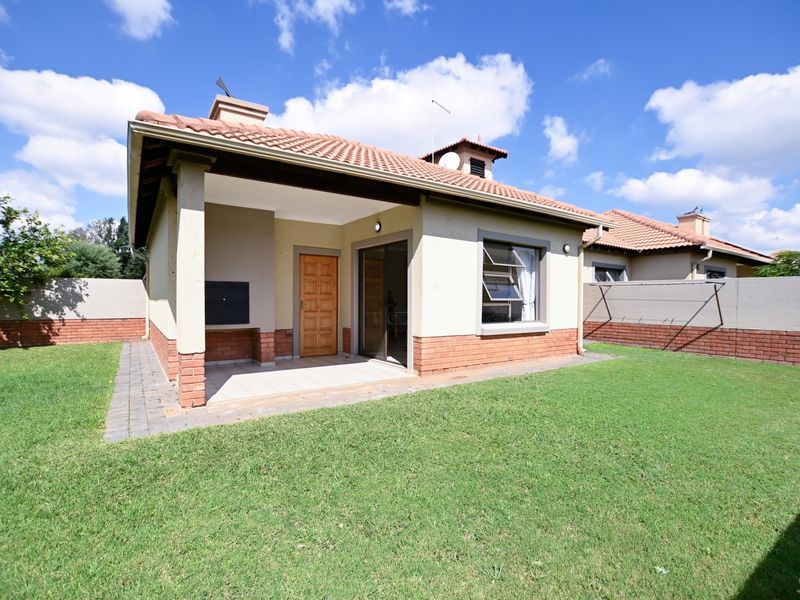 Rear view of the townhouse featuring a covered patio with a built-in braai, a private garden, and brick boundary walls.