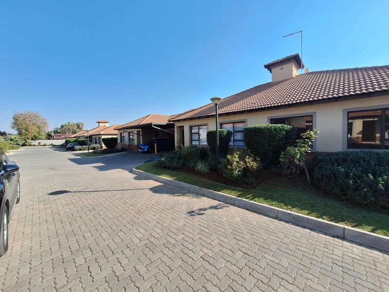 Front exterior view of a townhouse complex featuring paved driveways, tiled roofing, and established garden landscaping.