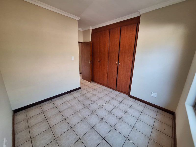 An empty bedroom featuring tiled flooring, neutral walls, and built-in wooden cupboards, offering a blank canvas for personalization.