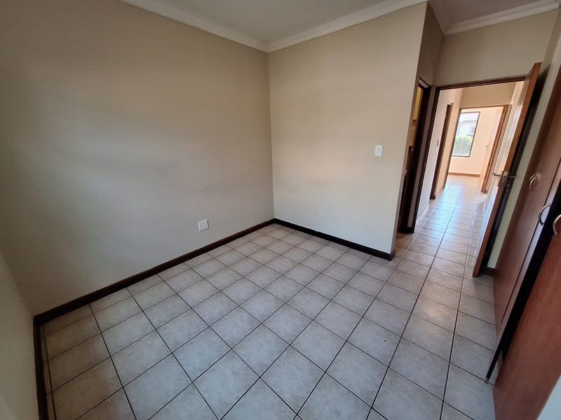 An empty bedroom featuring neutral wall paint, tiled flooring, and coving, with an adjacent hallway leading to another room.