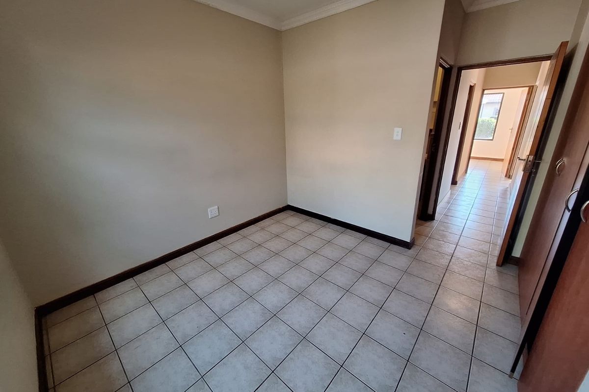 An empty bedroom featuring neutral wall paint, tiled flooring, and coving, with an adjacent hallway leading to another room.